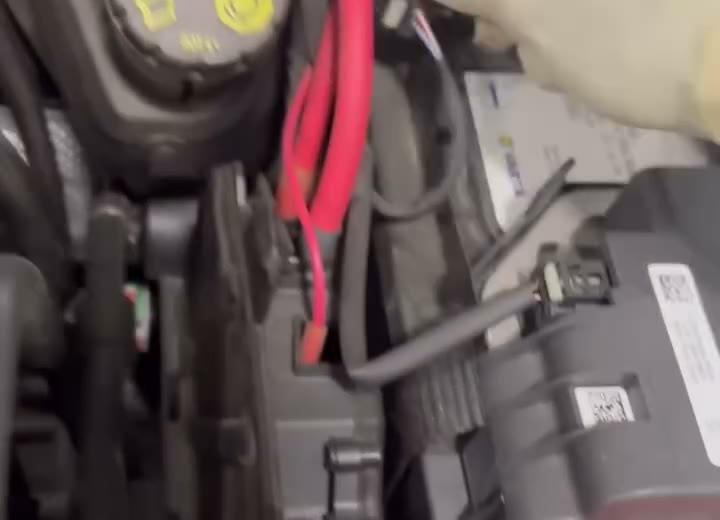 A battery terminal and red positive cable in an engine bay during electrical work.