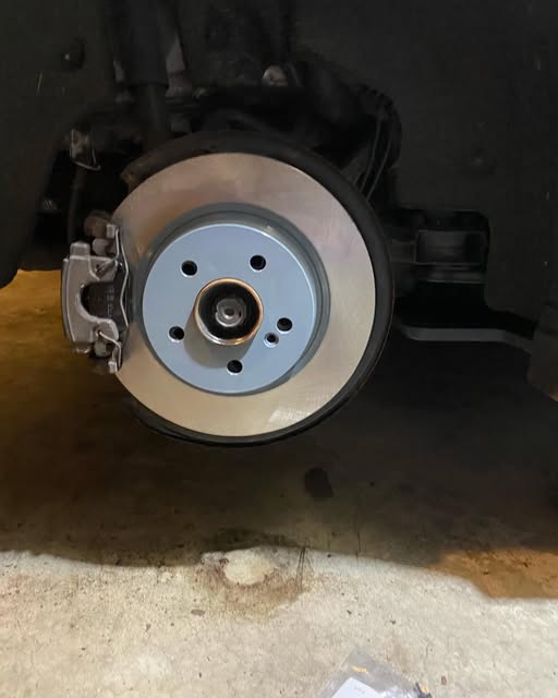 A brake rotor and caliper resting on concrete during an on-location brake service.