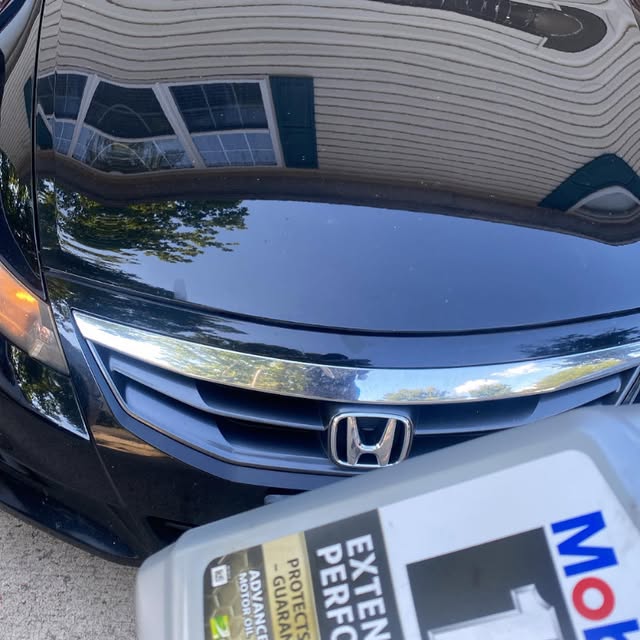 An oil service underway on a car bonnet with the oil container beside it.